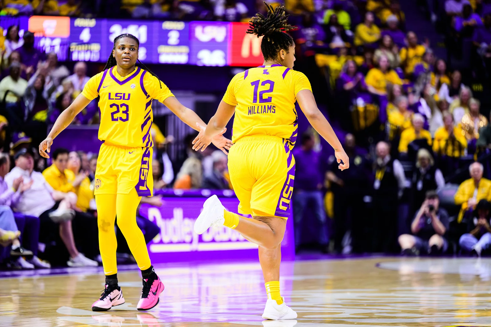Two LSU women's basketball players in yellow uniforms exchanging a celebratory hand slap on court
