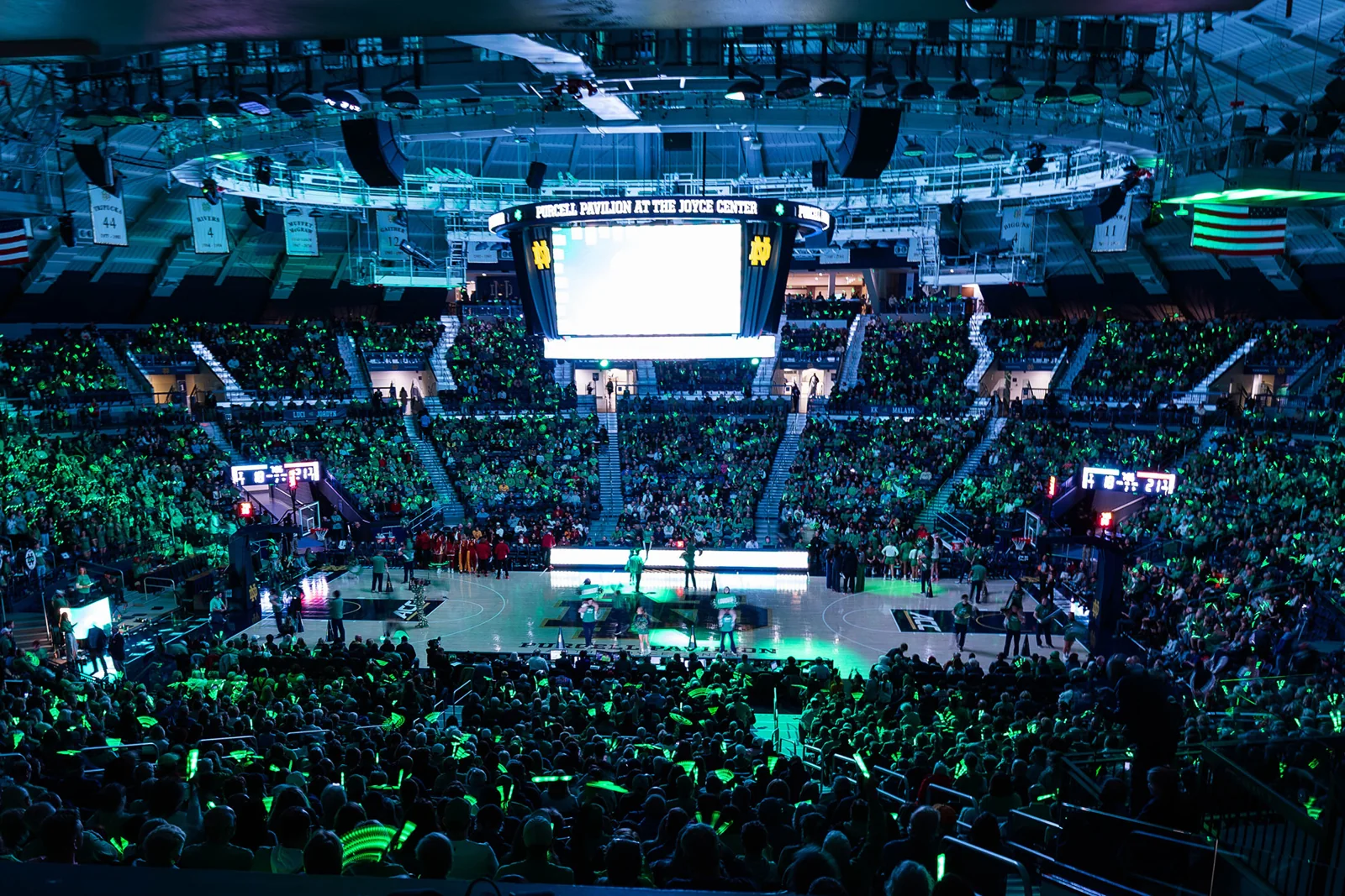 A packed Notre Dame basketball arena with the central scoreboard suspended above the court