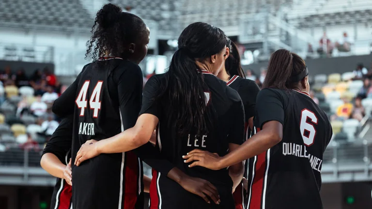 South Carolina women's basketball players in black uniforms standing arm in arm in a huddle