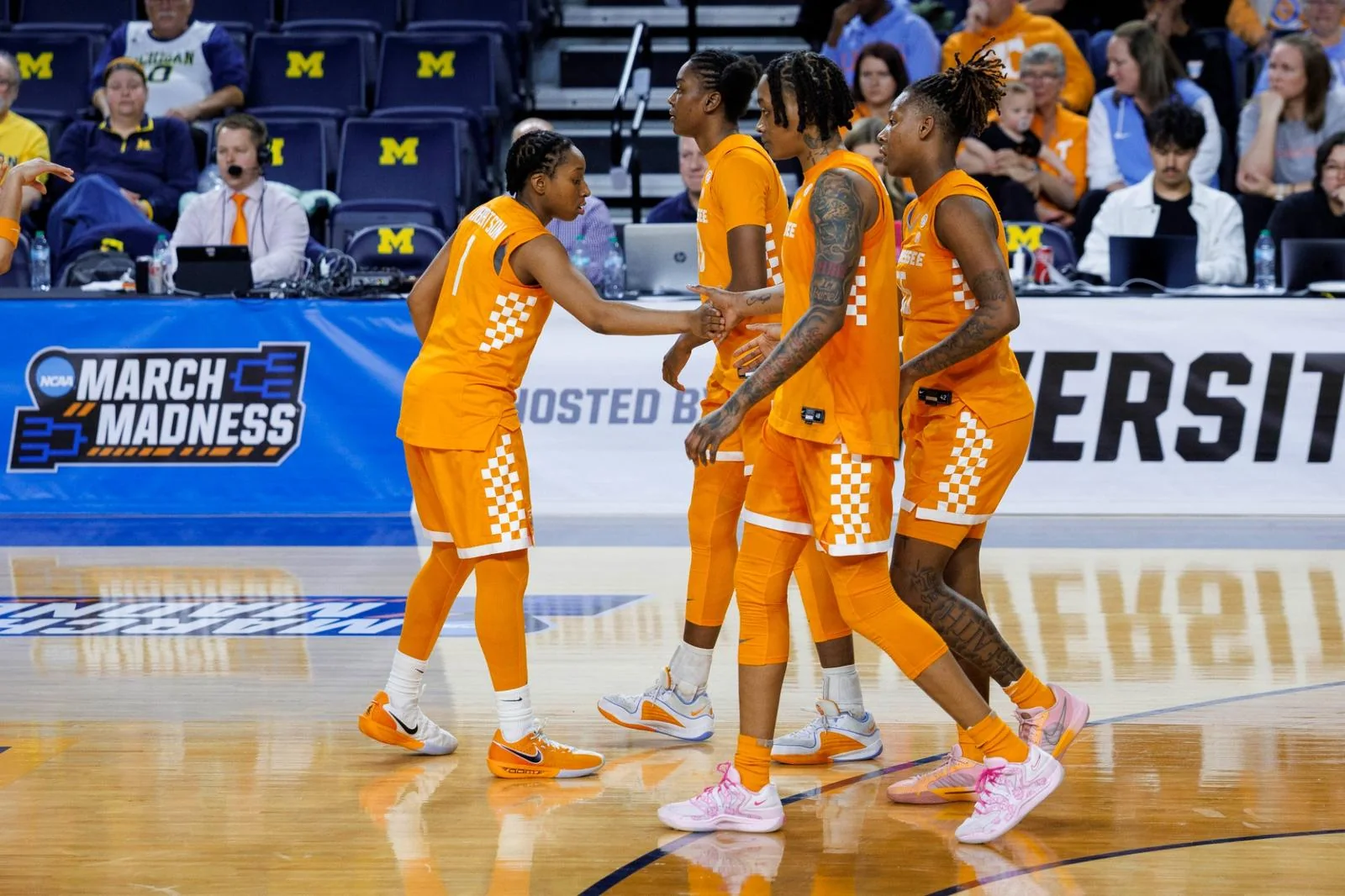 Tennessee Lady Vols players in orange uniforms meeting on court with a March Madness sign behind them