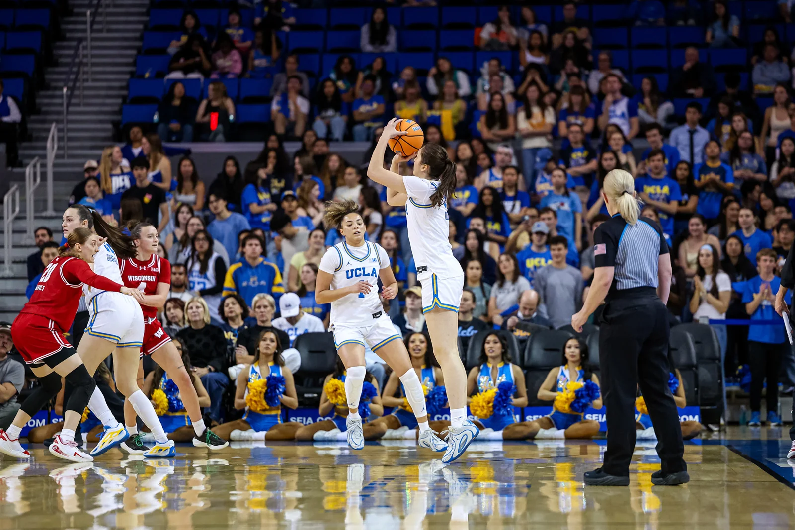 UCLA women's basketball player taking a jump shot in a white uniform as defenders close in