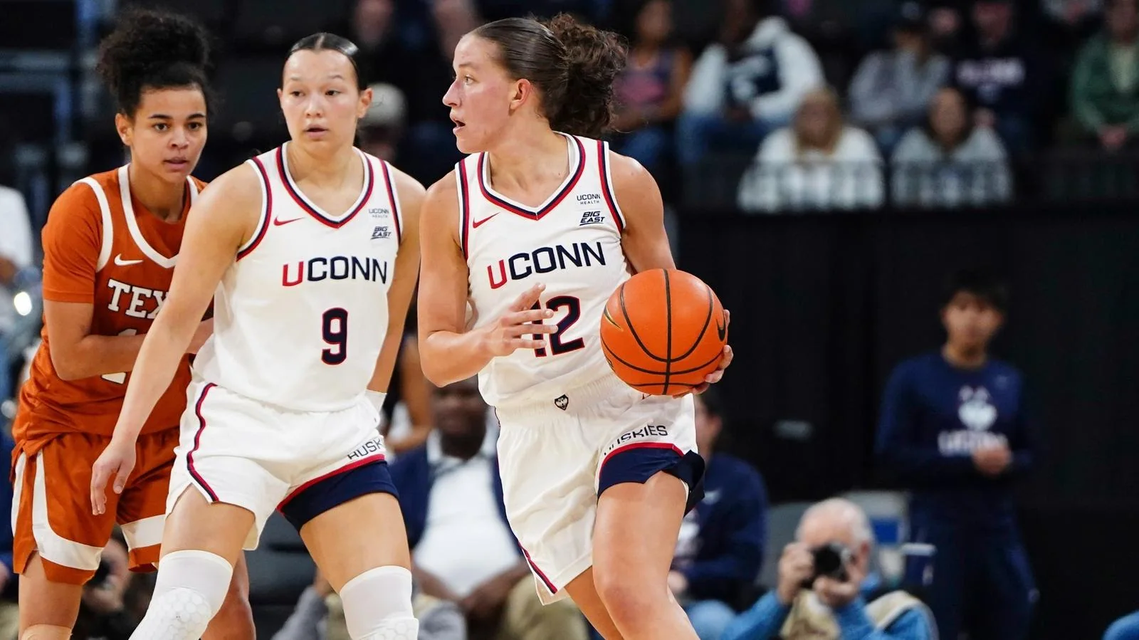 UConn women's basketball player dribbling beside a teammate while a Texas defender follows