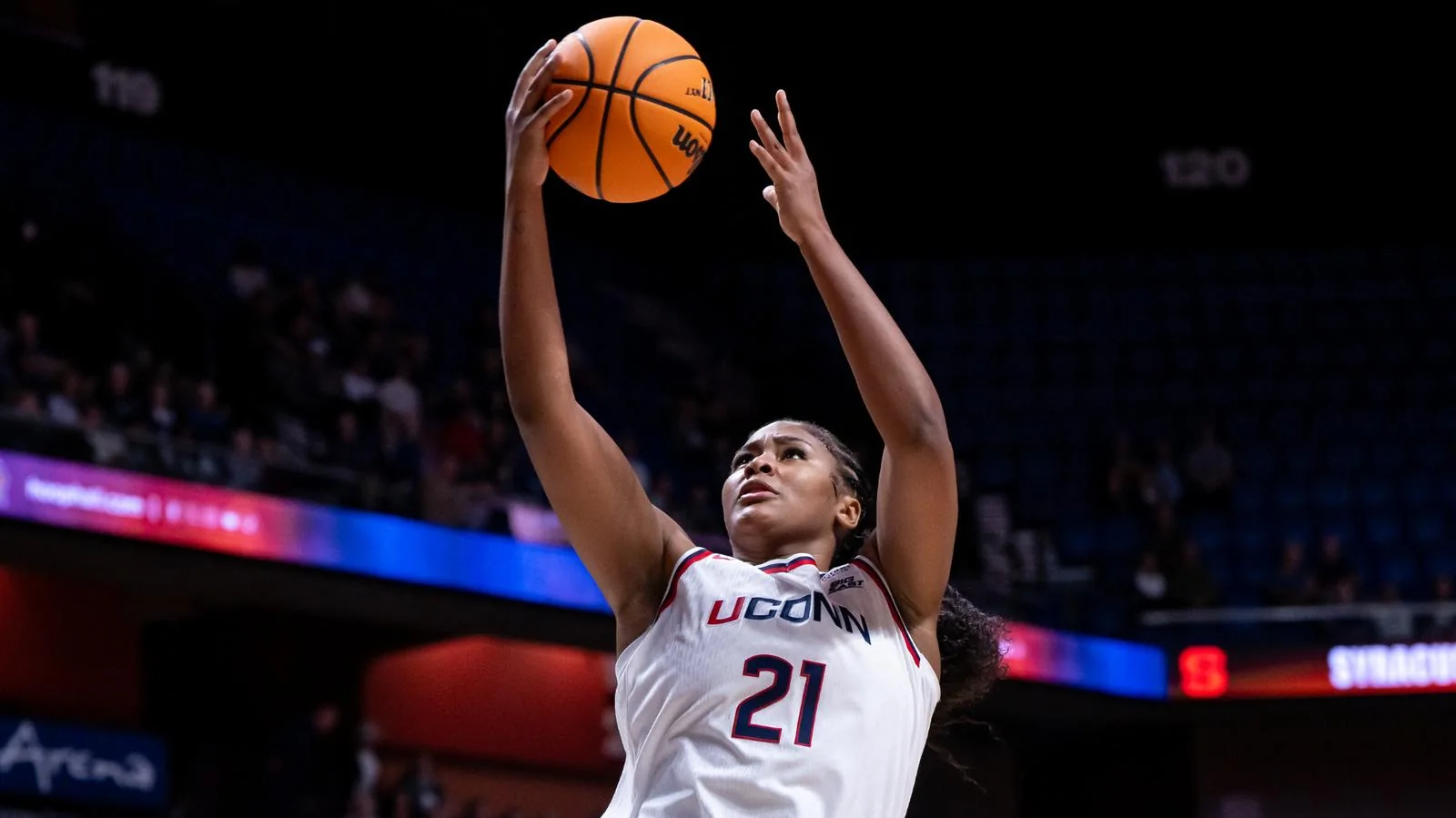 UConn women's basketball player in a white number 21 jersey extending one arm toward the basket with the ball