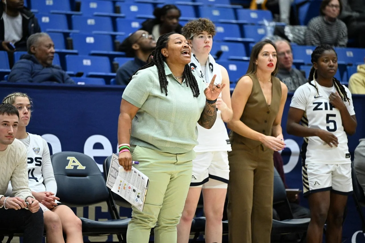 Akron Zips women's basketball: coach speaking to players beside the team bench