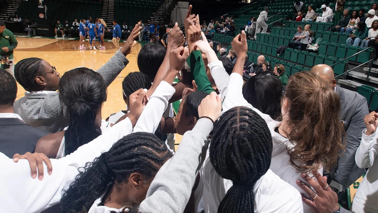Charlotte 49ers women's basketball: players raising their hands together in a team huddle