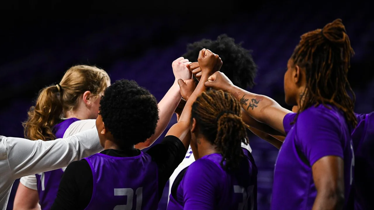 James Madison Dukes women's basketball: players joining hands in a team huddle
