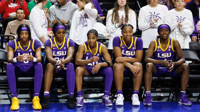 Five LSU Tigers players seated together on the bench in their purple jerseys