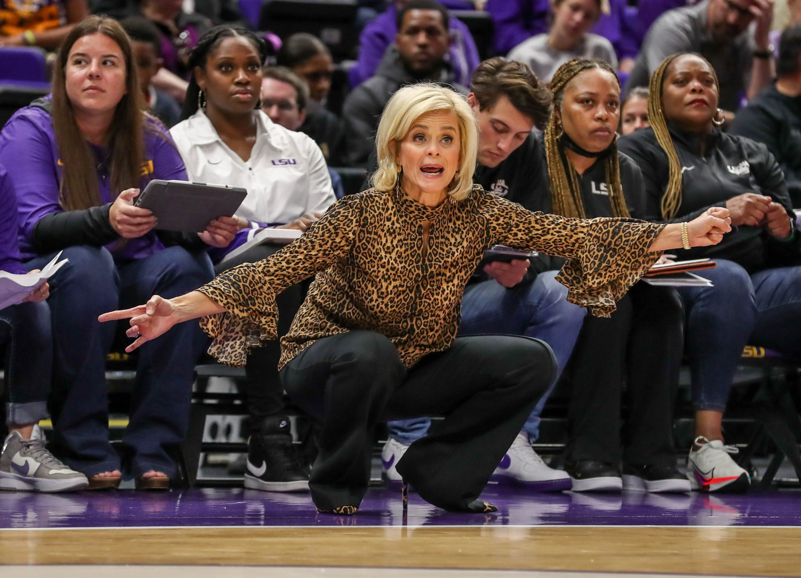 LSU head coach Kim Mulkey crouching and reacting animatedly from the sideline during a game