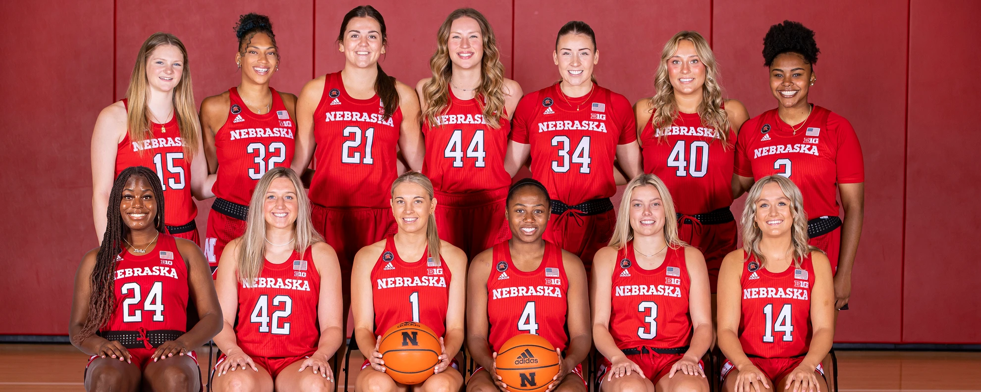 Nebraska Cornhuskers women's basketball team photo with players seated and standing in red jerseys against a red backdrop
