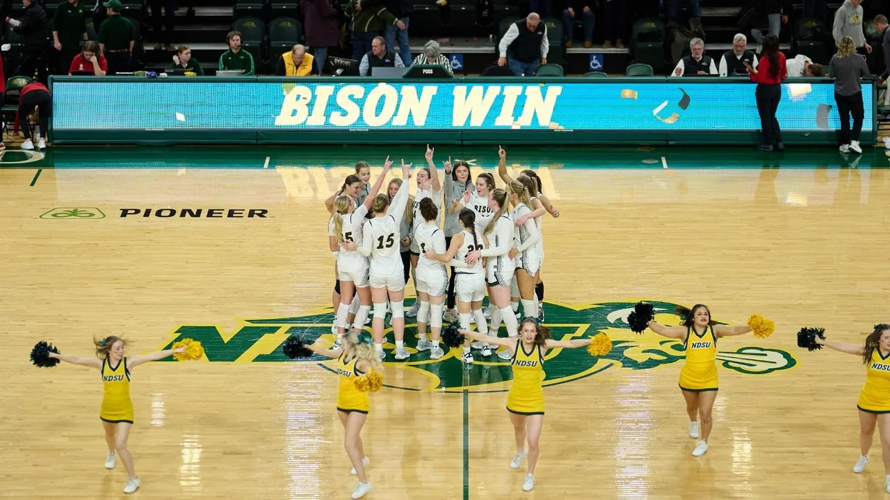 North Dakota State Bison women's basketball: players gathering on the home court beneath a Bison Win display