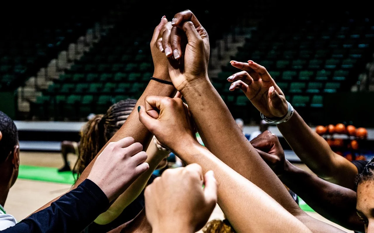 North Texas Mean Green women's basketball: players raising their hands together in a team huddle