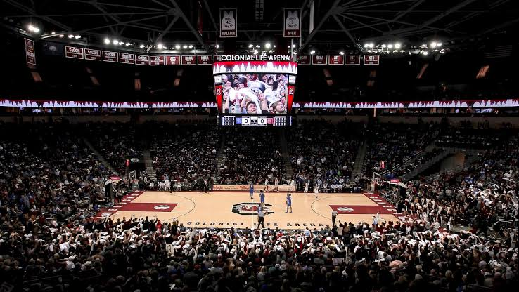 A sold-out Colonial Life Arena crowd during a South Carolina Gamecocks home game, with championship banners hanging above the court