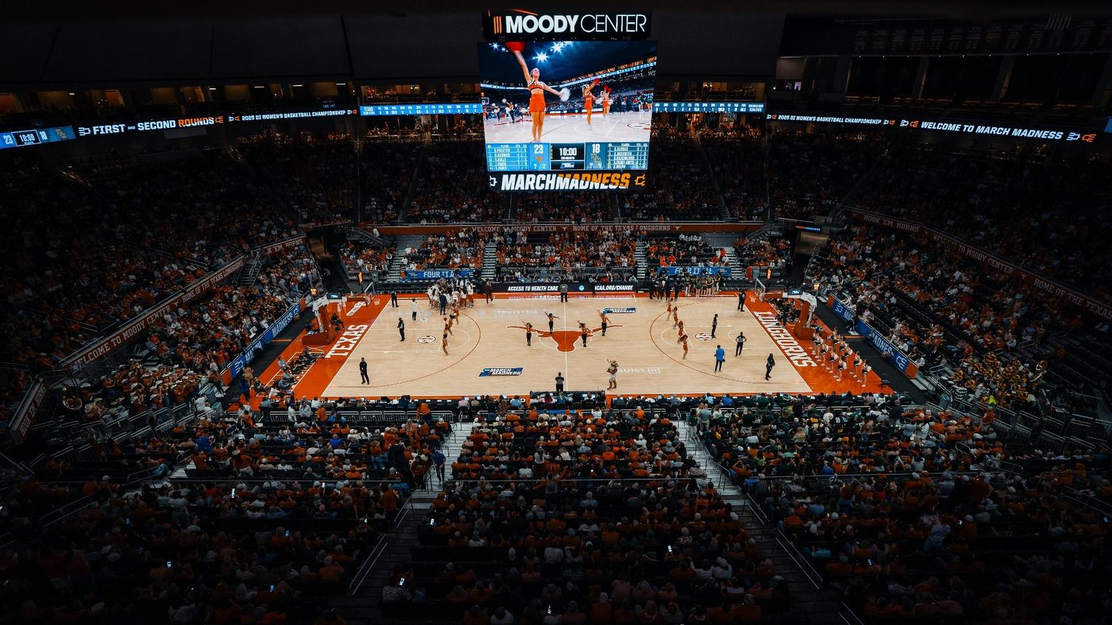 Wide view of the Moody Center packed for an NCAA Tournament March Madness game with the scoreboard showing the live score
