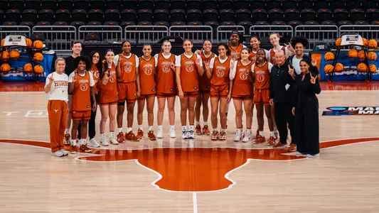 Texas Longhorns women's basketball team and staff posing together at center court inside the Moody Center