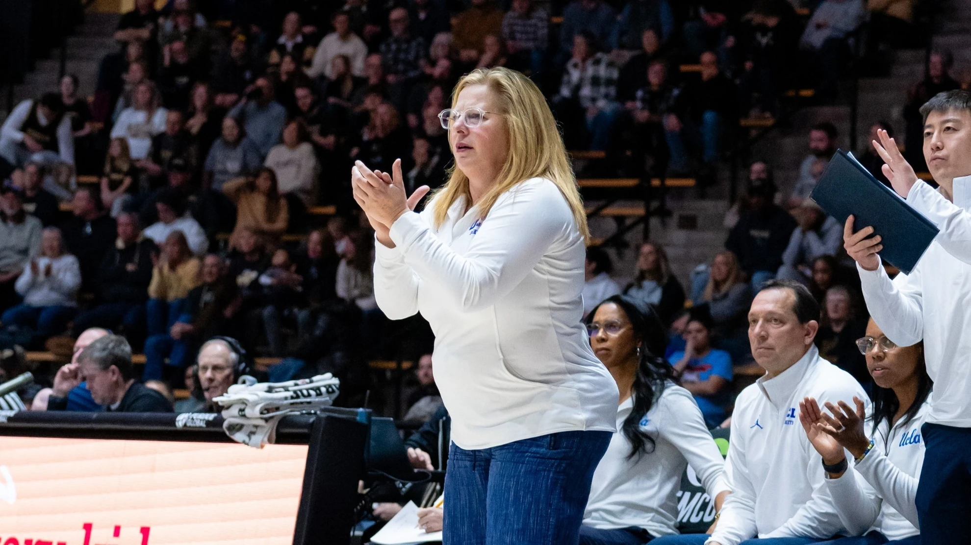 A UCLA assistant coach applauding from the sideline alongside the rest of the coaching staff during a game