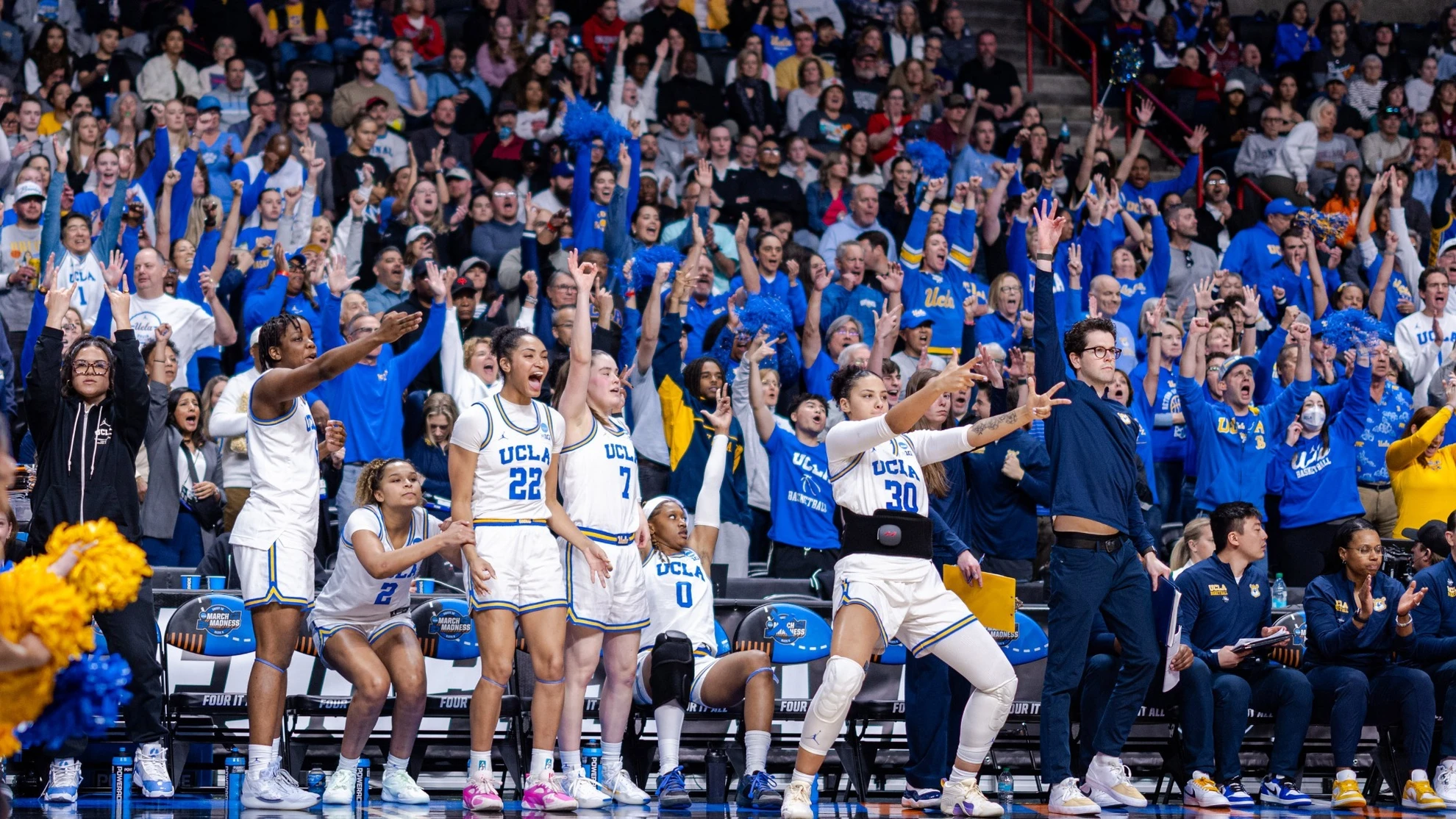 UCLA Bruins bench players celebrating with a cheering crowd behind them during an NCAA Tournament game