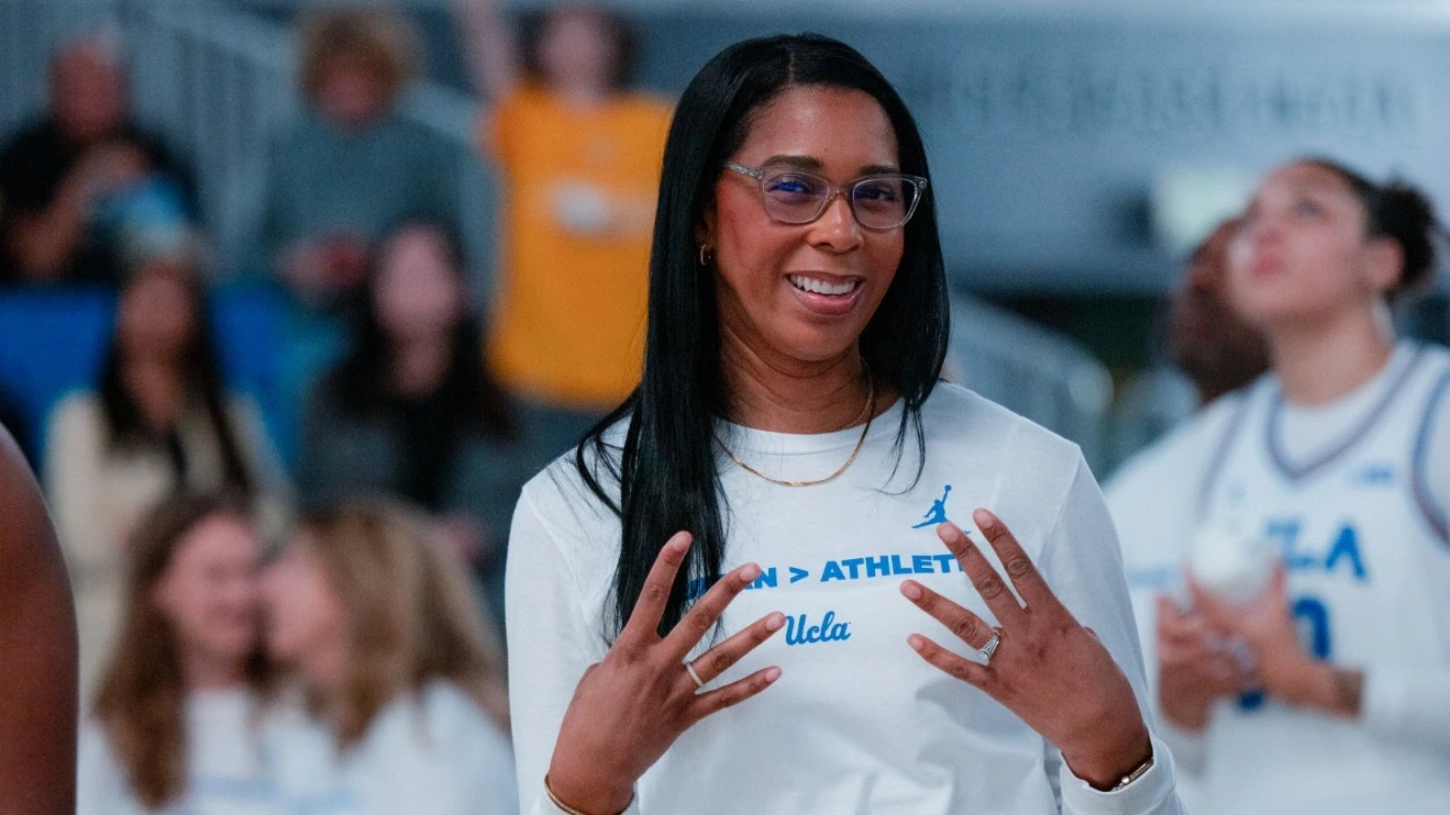 UCLA head coach Cori Close smiling and gesturing courtside in UCLA gear during a celebration