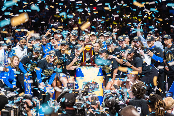 UCLA Bruins players and staff celebrating with the NCAA National Championship trophy under confetti after winning the 2026 title