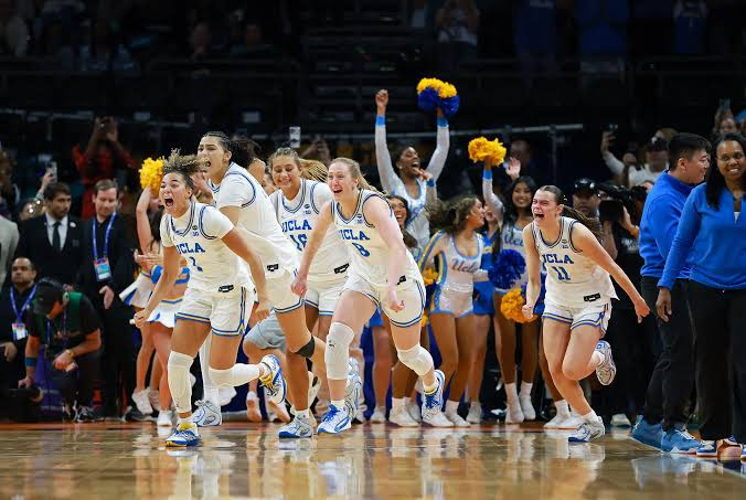 UCLA Bruins players running onto the court in celebration as cheerleaders wave pom-poms behind them