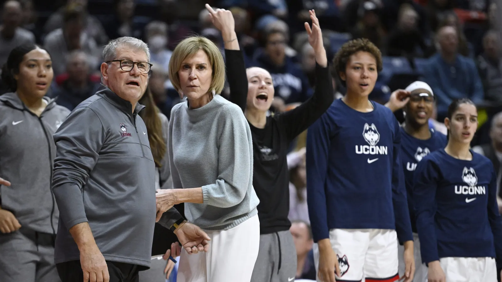 UConn head coach Geno Auriemma and an assistant coach reacting from the bench as players celebrate behind them