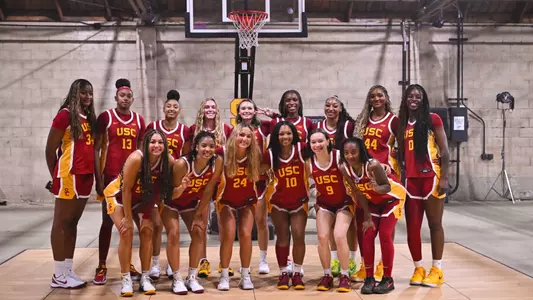 USC Trojans women's basketball team posing together in the practice gym in maroon and gold jerseys